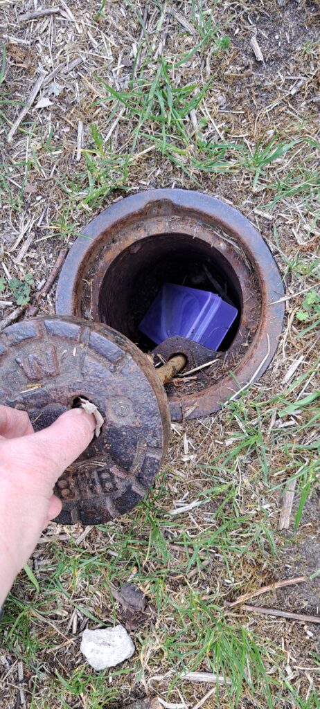 Geocache, im Boden versteckt in einem kleinen Fake Kanaldeckel