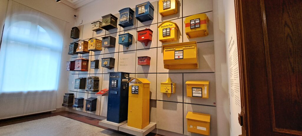 An einer Wand hängen alte und neue Briefkästen aus verschiedenen Zeiten und Ländern
