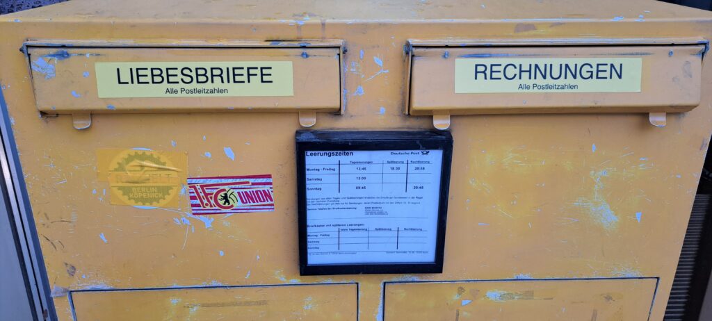 Briefkasten mit zwei Einwürfen, auf denen jeweils ein gelber Aufkleber mit links Liebesbriefe und rechts Rechnungen klebt.