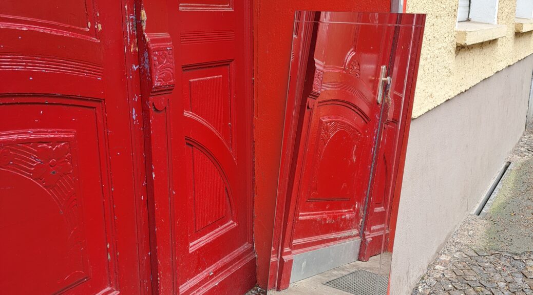 Rote Eingangstür aus Holz, die sich in einem Spiegel spiegelt, der zum Mitnehmen abgestellt wurde.