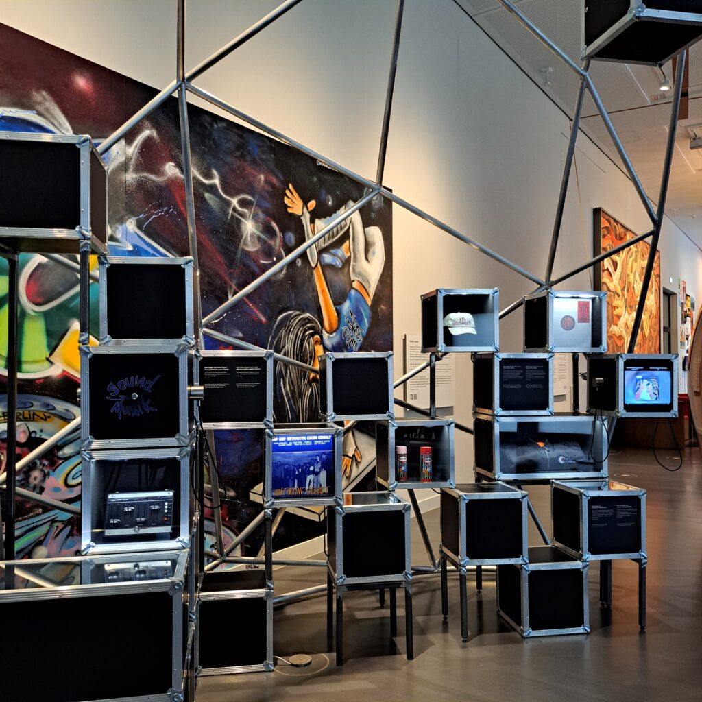 schwarze Kästen, in denen Geräte und Kleidung eines DJS gezeigt werden