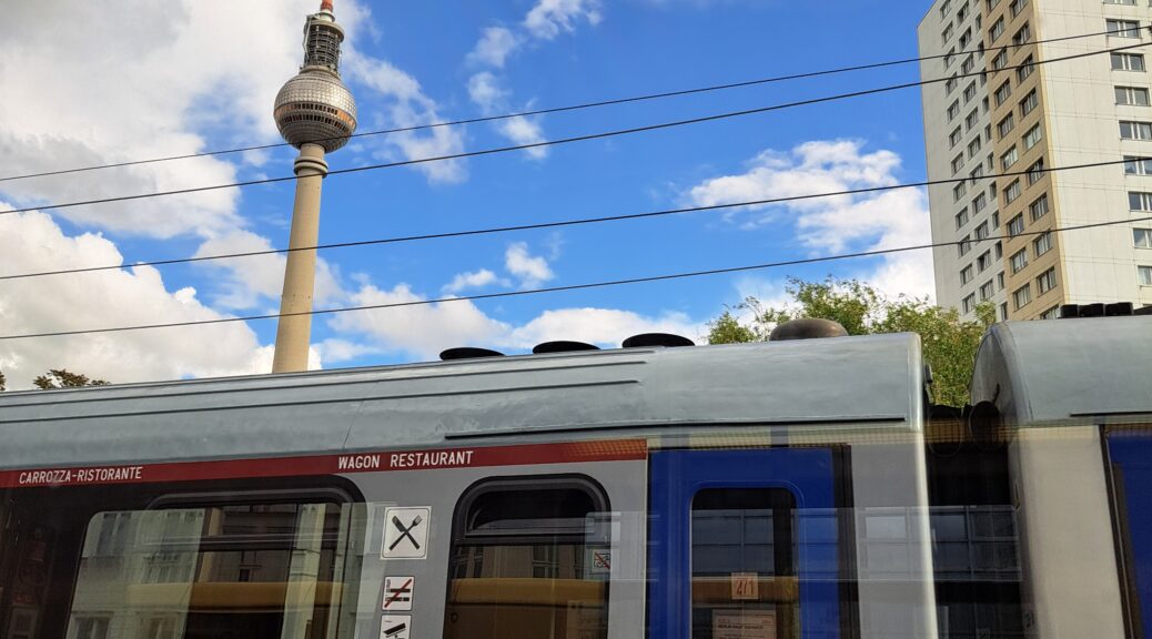 Zugwaggon im Vordergrund, Hintergrund Berliner Fernsehturm vor weißen Wolken, blauem Himmel